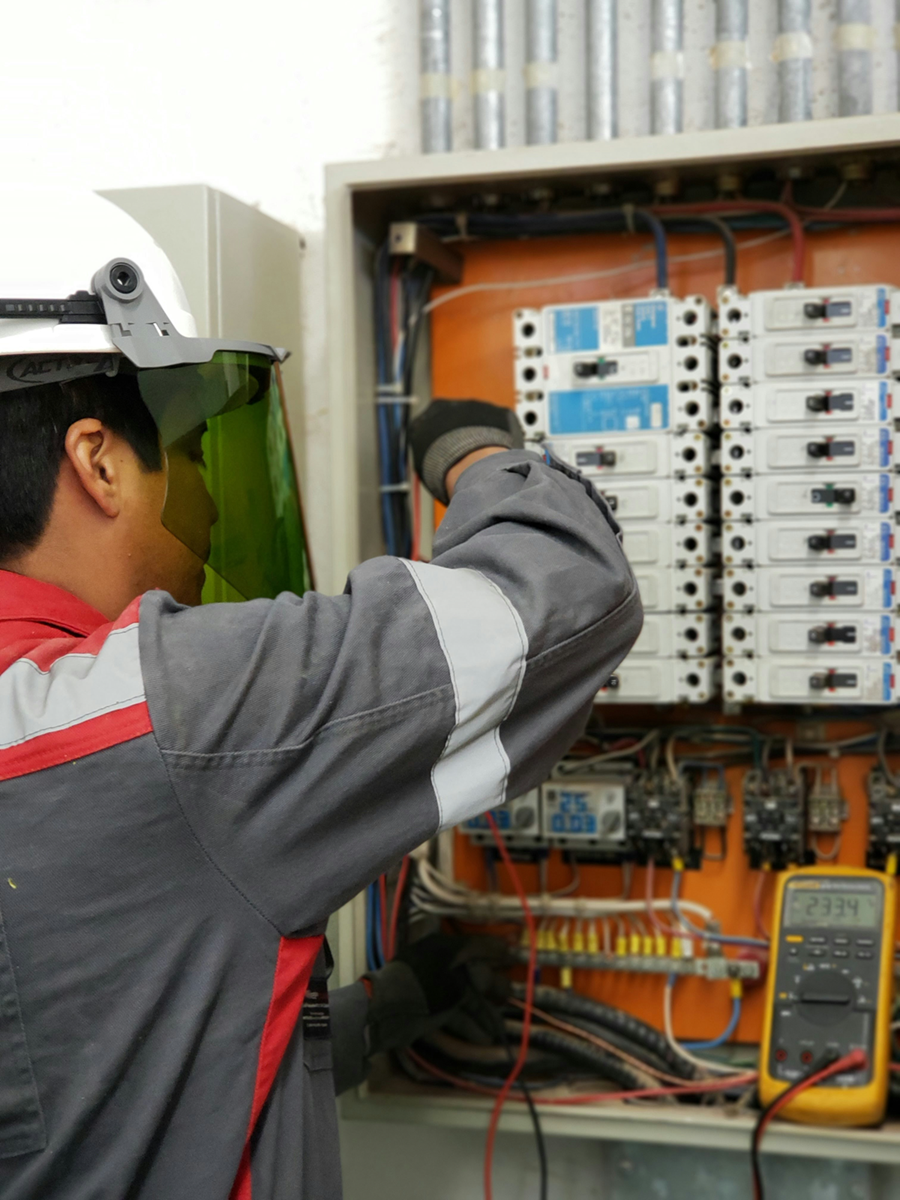 Commercial electrician inspecting industrial breaker panel with safety equipment
